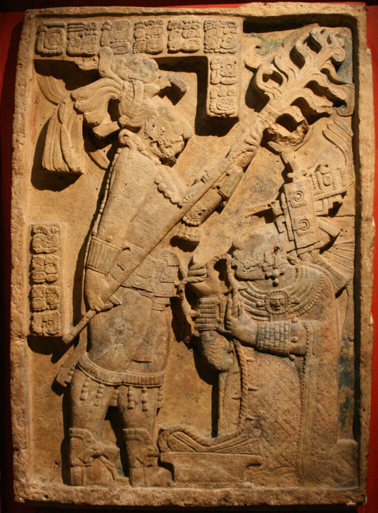 Maya King Bahlam III and Queen K'ab'al performing a bloodletting sacrifice. In the lintel, Lady K'ab'al is shown pulling a barbed rope through her tongue. She is sitting at the feet of the king, who is holding a sceptre clearly identifying his importance.