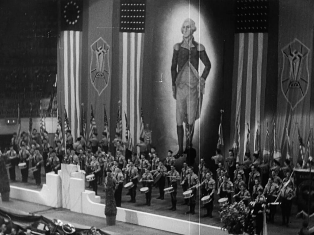 Photograph of a pro-Nazi Bund held in Madison Square Garden, New York, 1939. Although George Washington is shown prominently on the screen in the background, Nazi flags flank the stage. Shown in the front are drummers on a stage.