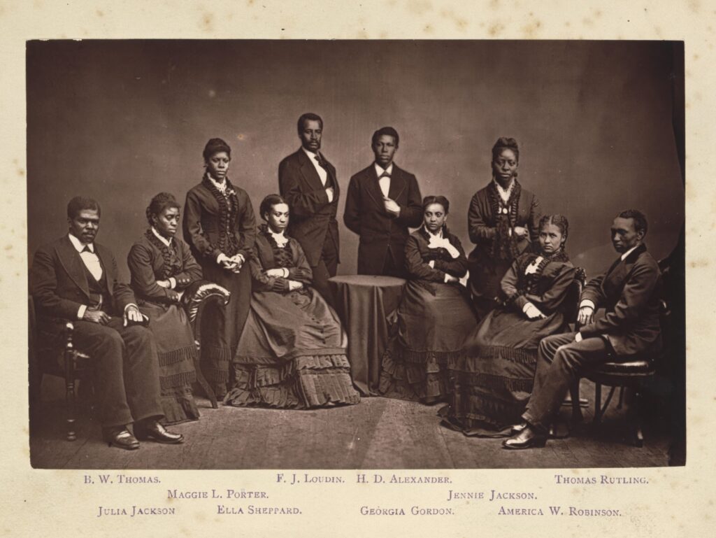 These ten a capella singers from Fisk University popularized spirituals as they toured the country. Six students are seated and four stand in the background. All are dressed in black-and-white formal wear. Across the bottom is the names of the students. On the top line, "B. W. Thomas, F.J. Loudin, H.D. Alexander, Thomas Rutling." On the next line, it reads, "Maggie L. Porter. Jennie Jackson. Finally, on the last row, the names "Julia Jackson, Ella Sheppard, Georgia Gordon, and America W. Robinson" are found.
