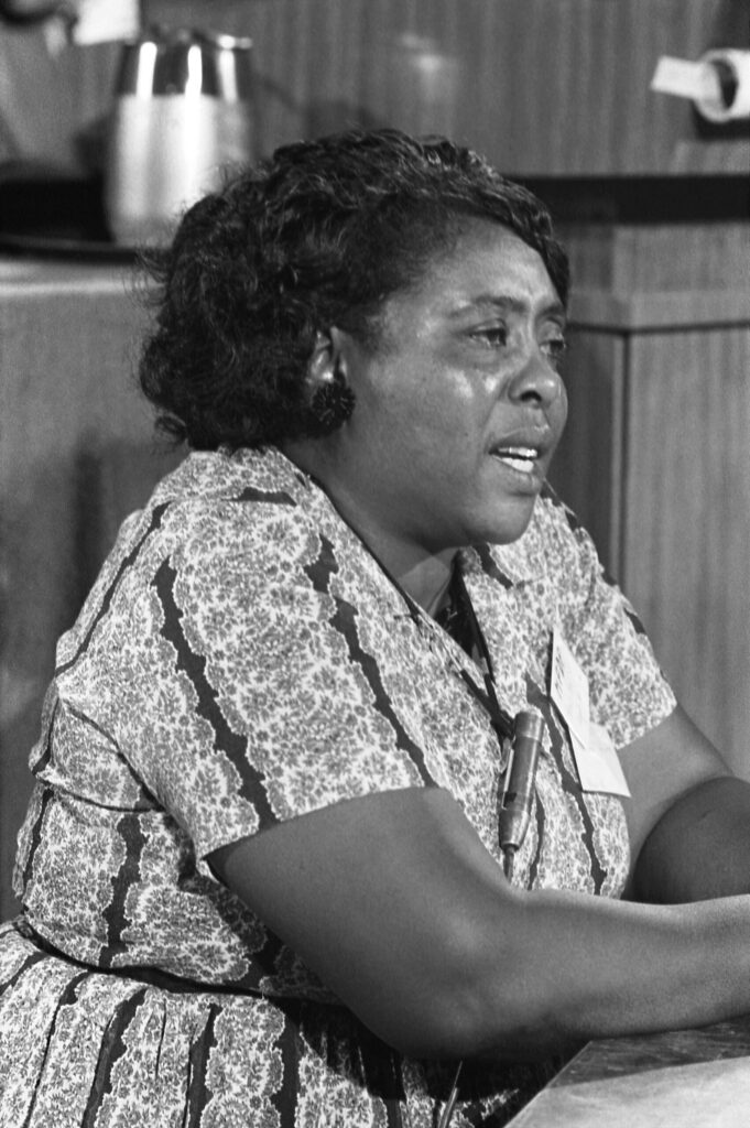 Famous Civil Rights activist Fannie Lou Hamer, pictured with her arms folded on a table and speaking into a microphone.