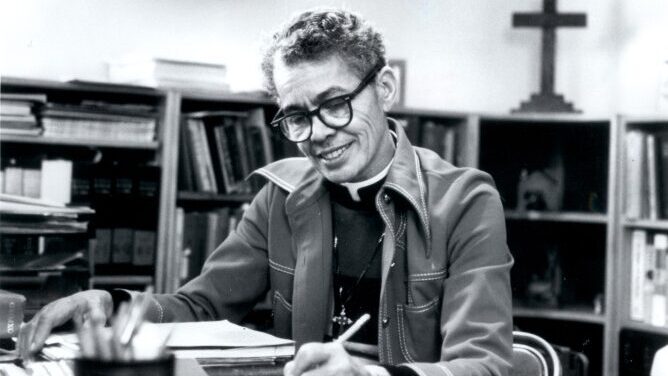 Activist, legal scholar, and Episcopalian minister Anna Pauline "Pauli" Murray is shown working in a library or archive and has short, curly hair and black-rimmed glasses. In the back right corner of the black-and-white photograph is a cross prominently displayed and bookshelves filled with manuscripts.