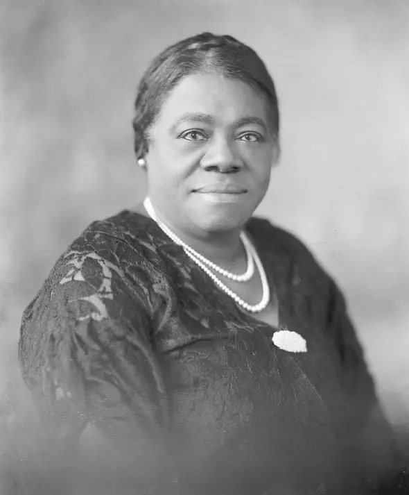 Mary McLeod Bethune is shown seated in a dark lace dress and white pearl necklace and earrings.