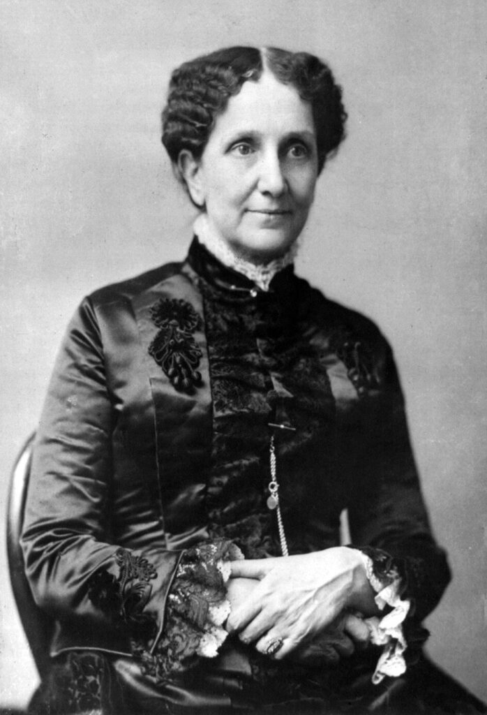 Photograph of Mary Baker Eddy dressed in a beautiful, embellished silk dress, lace around the neckline and arms. Eddy's hair is crimped and tied into an updo.