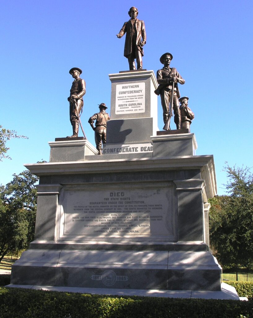 A monument to the memory of dead Confederate soldiers and the "Lost Cause." Four bronze men stand watch on the four corners, while a Jefferson Davis statue is shown at the top. Beneath is the phrase, 
"SOUTHERN CONFEDERACY
Formed by following states withdrawing from the Union
South Carolina 
December twentieth 
Eighteen Hundred and Sixty."

An inscription at the base of the first part, reads "CONFEDERATE DEAD."

The second section of the statue bears the inscription:
"FOR STATES RIGHTS

GUARANTEED UNDER THE CONSTITUTION

THE PEOPLE OF THE SOUTH, ANIMATED BY THE SPIRIT OF 1776, TO PRESERVE THEIR RIGHTS,

WITHDREW FROM THE FEDERAL COMPACT IN 1861. THE NORTH RESORTED TO COERCION.

THE SOUTH, AGAINST OVERWHELMING NUMBERS AND RESOURCES,

FOUGHT UNTIL EXHAUSTED,

DURING THE WAR THERE WERE TWENTY TWO HUNDRED AND FIFTY SEVEN ENGAGEMENTS;
IN EIGHTEEN HUNDRED AND EIGHTY TWO OF THESE, AT LEAST ONE REGIMENT TOOK PART.
NUMBER OF MEN ENLISTED:
CONFEDERATE ARMIES 600,000; FEDERAL ARMIES 2,859,132
LOSSES FROM ALL CAUSES
CONFEDERATE, 437,000; FEDERAL, 485,216.
1861 [a seal] 1865."