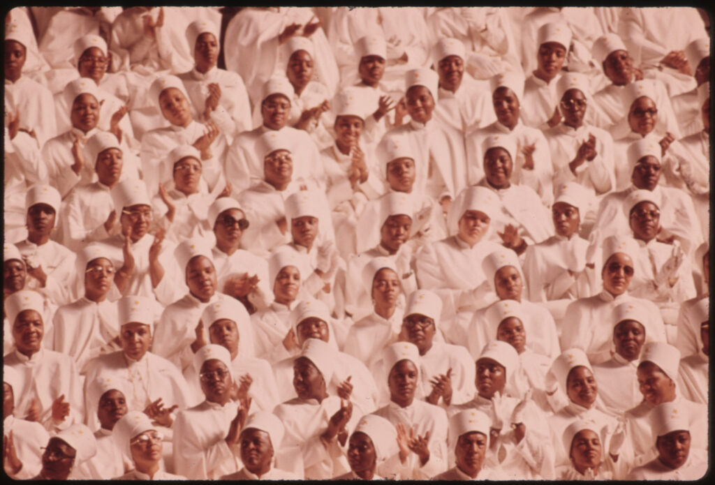 Black Muslim women dressed in white clothing and caps applaud during an address by Elijah Muhammad during the annual Savior's Day. 