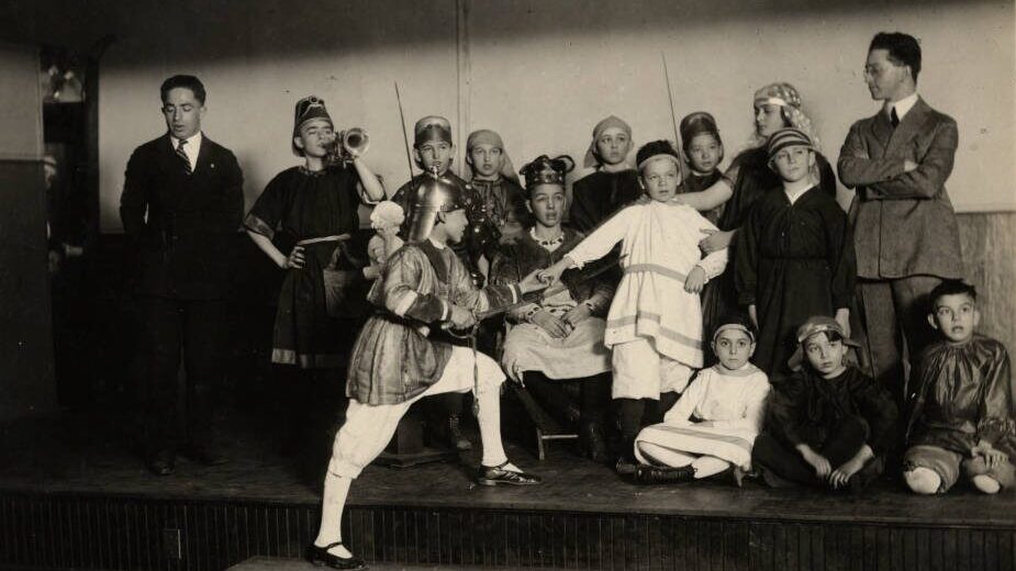 Students portray the Maccabees for a Hanukkah play in 1928 at the Capitol City Hebrew School in St Paul. Thirteen students wear black or white costumes and different headdresses. On the left and right are two male teachers.